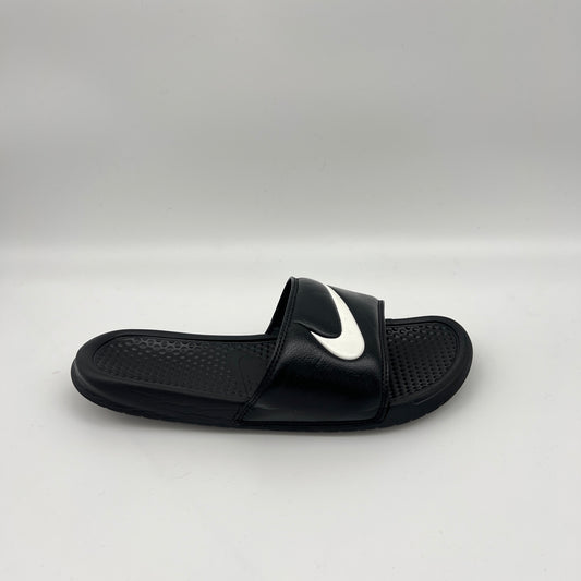 Side profile of a single black Nike Benassi Swoosh slide featuring a white Nike logo on the synthetic leather strap and a pebbled comfort footbed.
