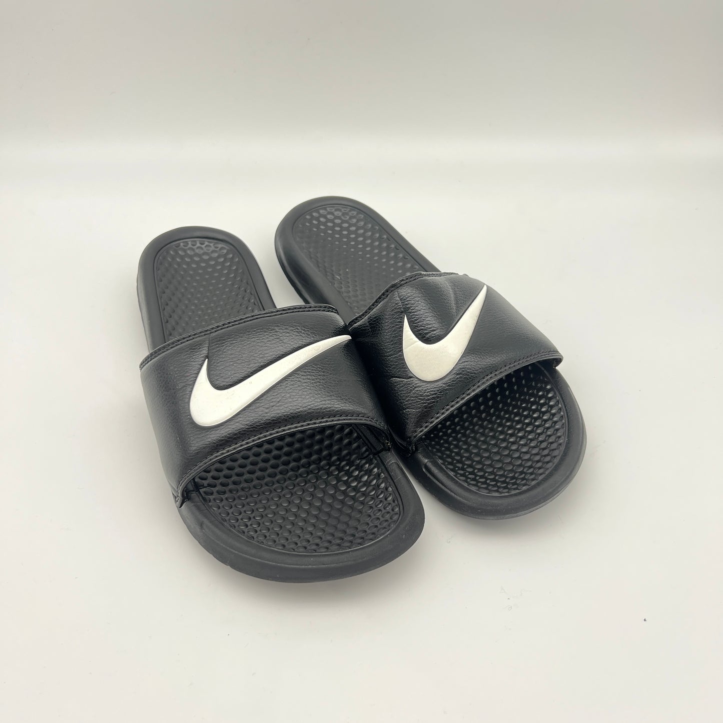 Black Nike slides with white logo on a light gray background