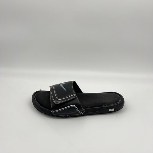 Side view of a single black Nike Comfort Slide 2 sandal with white stitching and a metallic silver Swoosh logo on an adjustable velcro strap