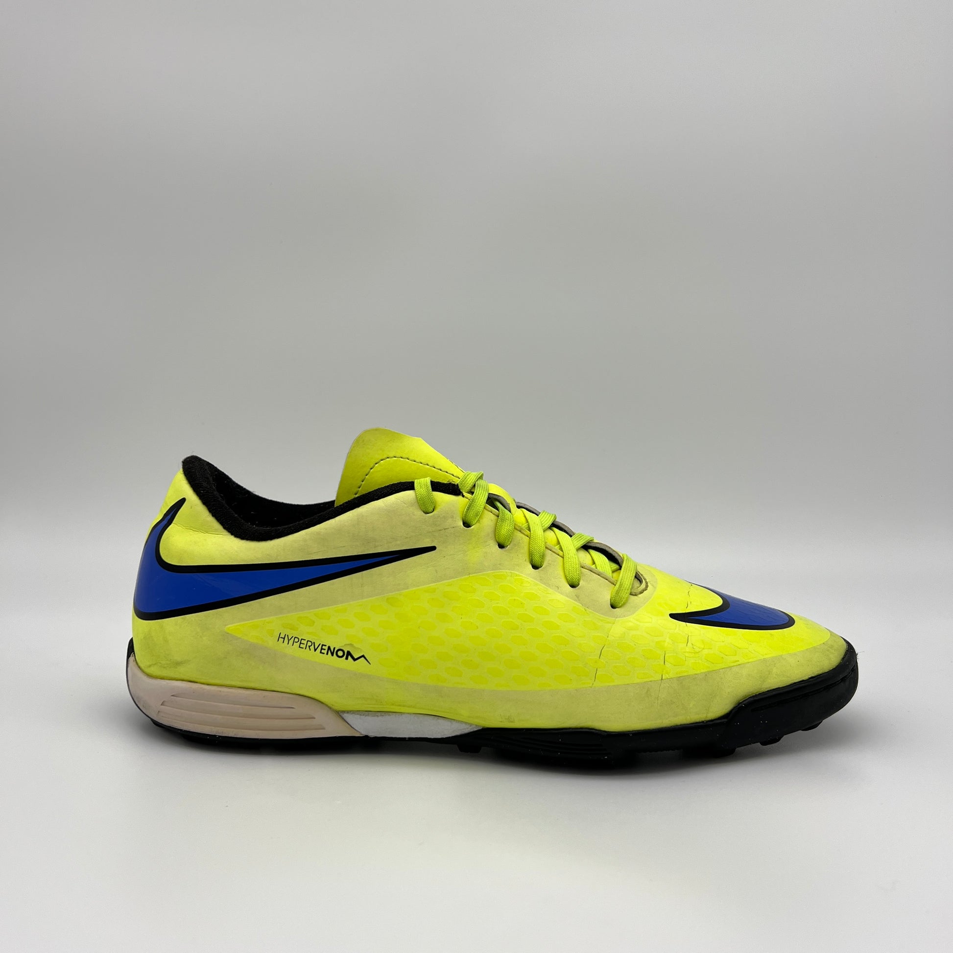 Side profile of a bright neon yellow (Volt) Nike Hypervenom turf soccer shoe with a purple swoosh and textured synthetic upper on a grey background.