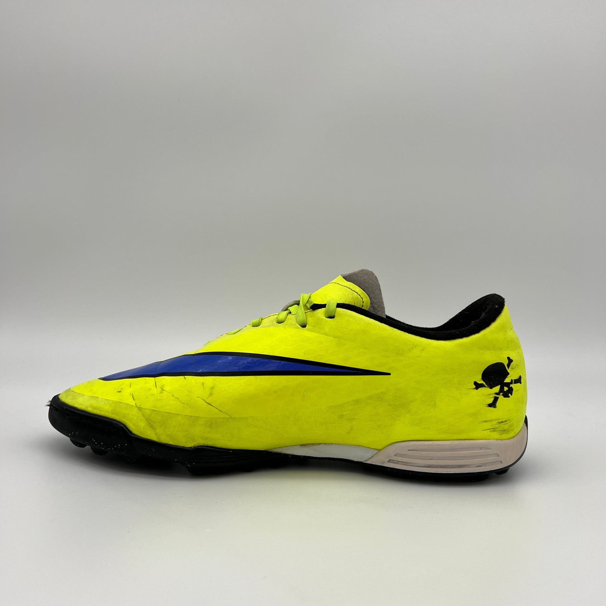 Side profile of a bright neon yellow (Volt) Nike Hypervenom turf soccer shoe with a purple swoosh and textured synthetic upper on a grey background.