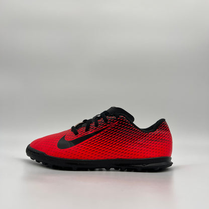 Profile view of a red and black Nike Jr. BravataX II (TF) turf soccer shoe with a black Nike swoosh and a multi-studded rubber outsole for artificial grass
