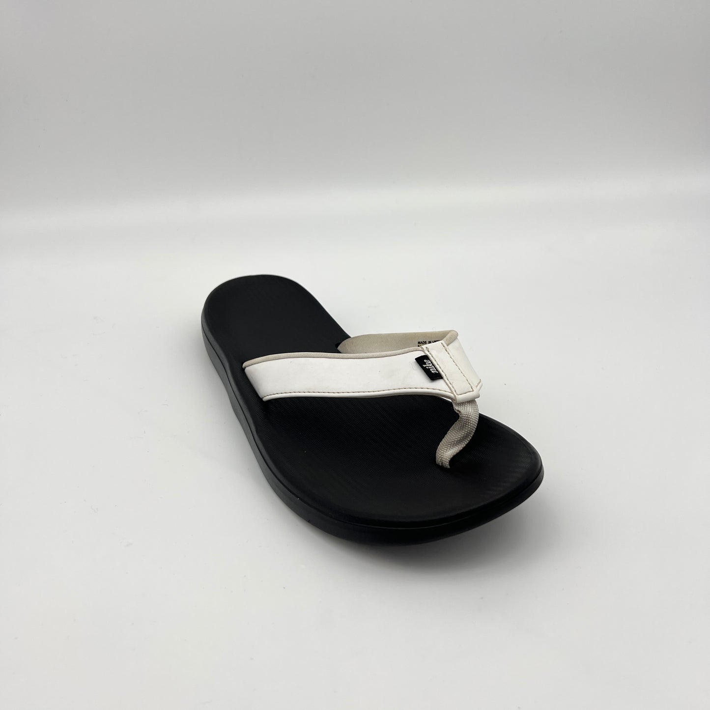 Black sandal with a white strap on a light gray background