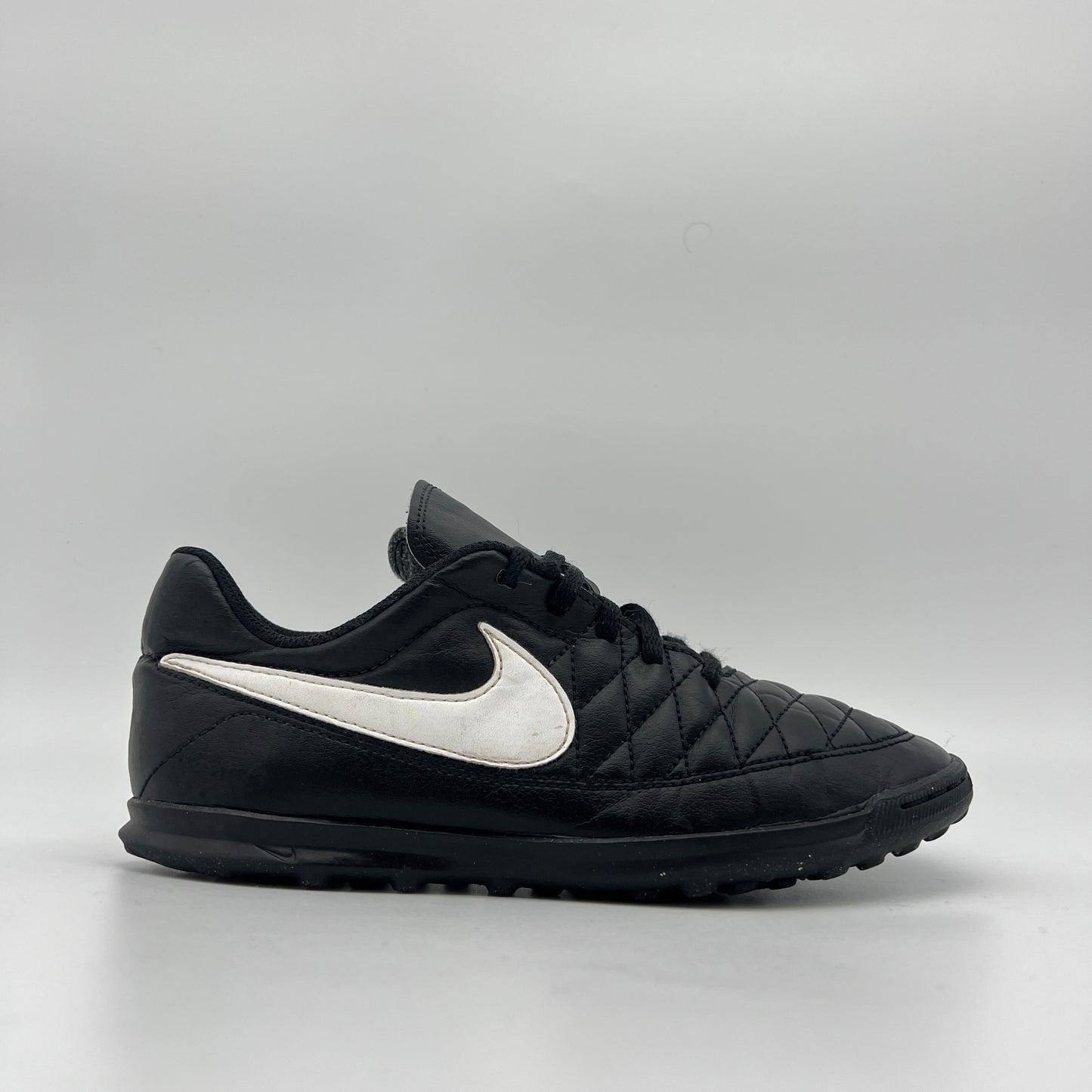 Black Nike Majestry IC indoor soccer shoe with a white swoosh and a classic quilted-style stitched upper on a white background.