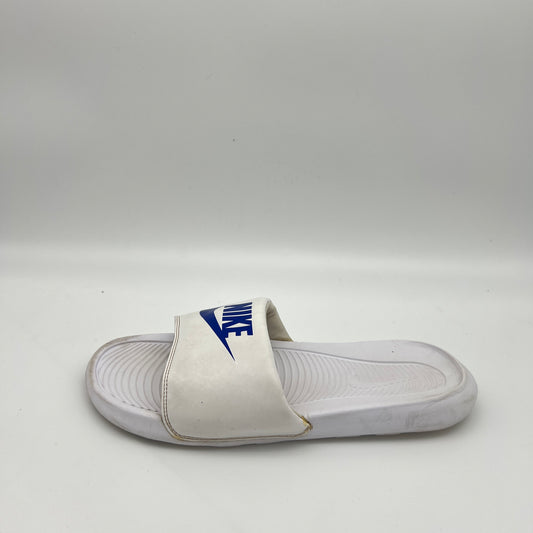 White Nike Victori One slide sandal with a royal blue Nike logo and swoosh on the padded strap, set against a white background.