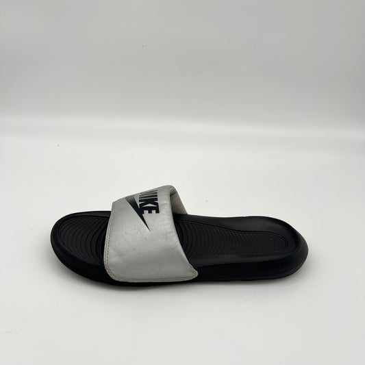 Metallic silver Nike Victori One slide sandal with a bold black Nike logo on the strap and a black contoured footbed.
