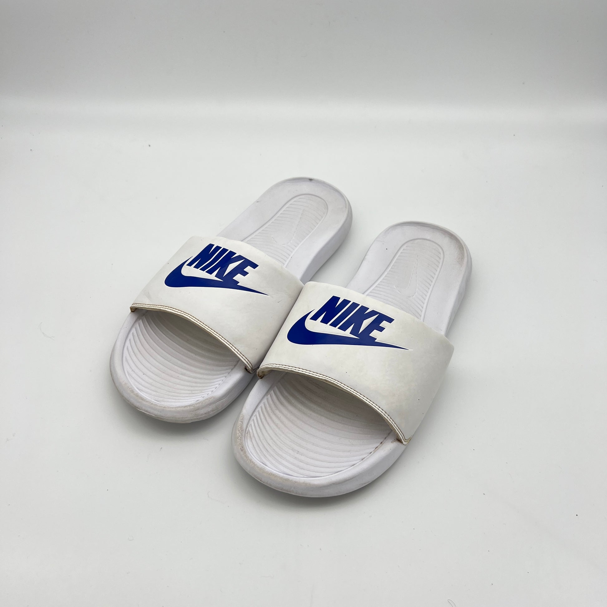 White Nike slides with blue logo on a white background