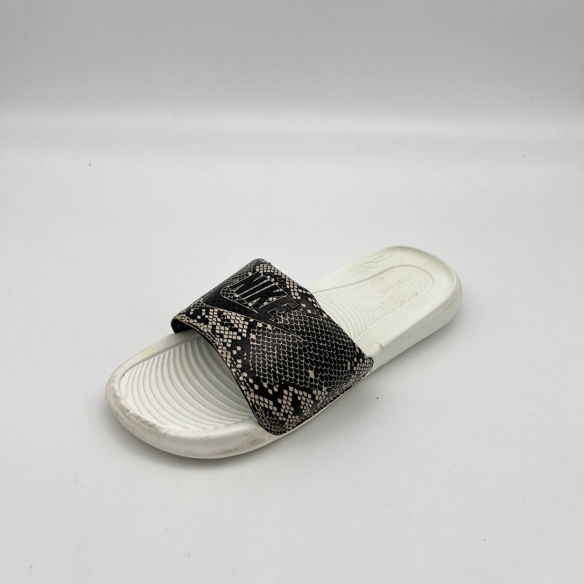 White slide sandal with black patterned strap on a light gray background