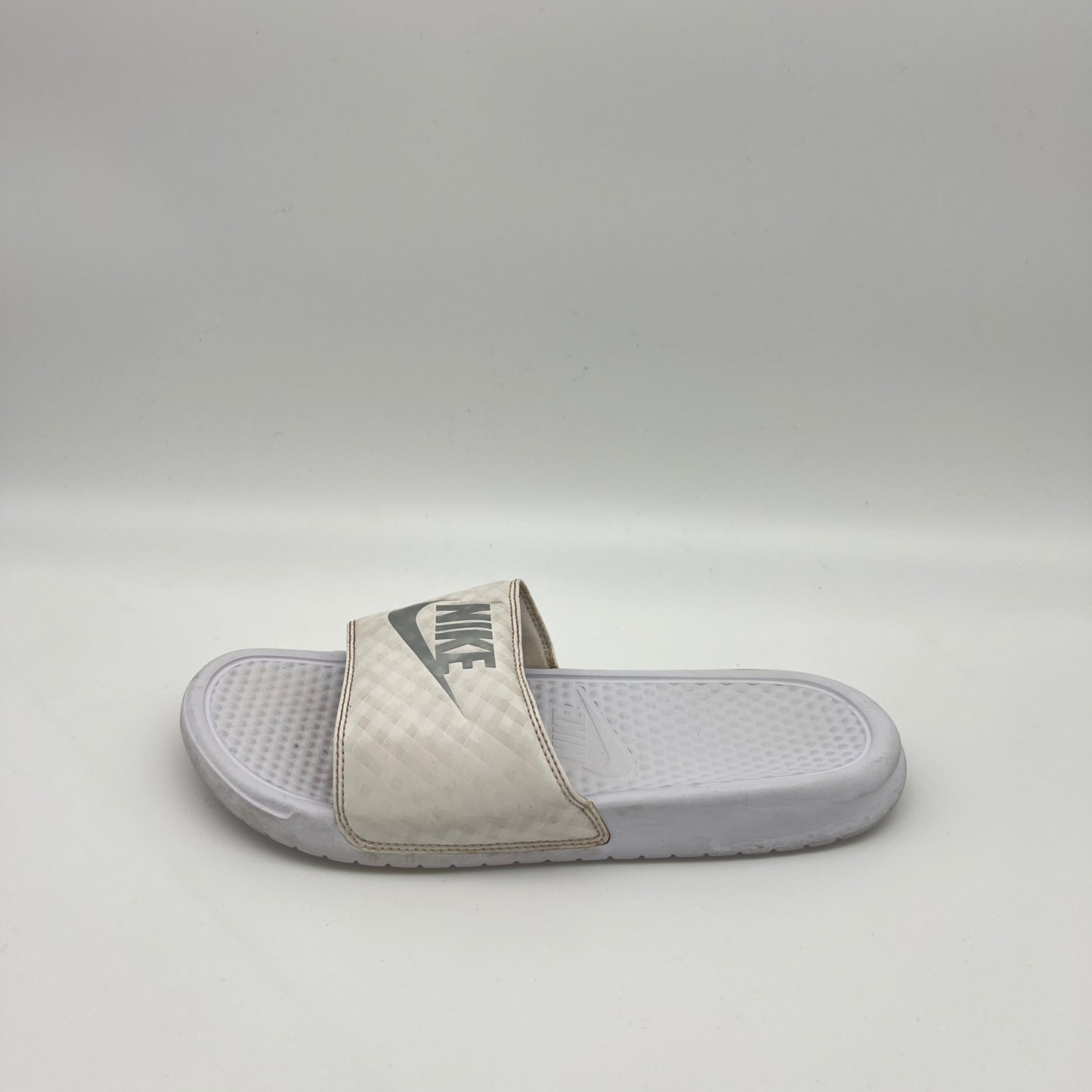 A single white Nike Benassi JDI slide sandal featuring a metallic silver Nike logo on a white checkered-patterned strap and a textured white footbed.