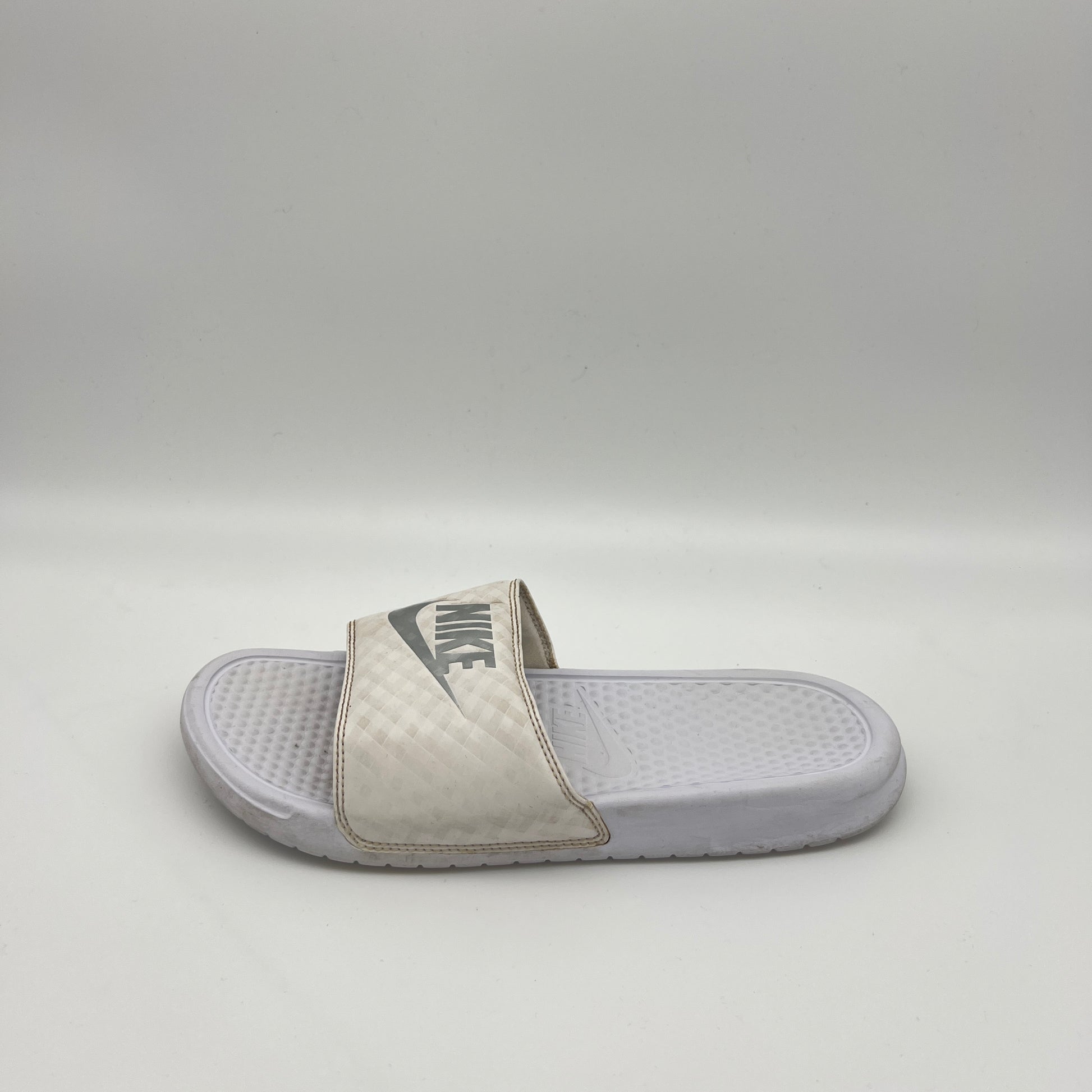 A single white Nike Benassi JDI slide sandal featuring a metallic silver Nike logo on a white checkered-patterned strap and a textured white footbed.