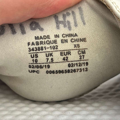 A single white Nike Benassi JDI slide sandal featuring a metallic silver Nike logo on a white checkered-patterned strap and a textured white footbed.
