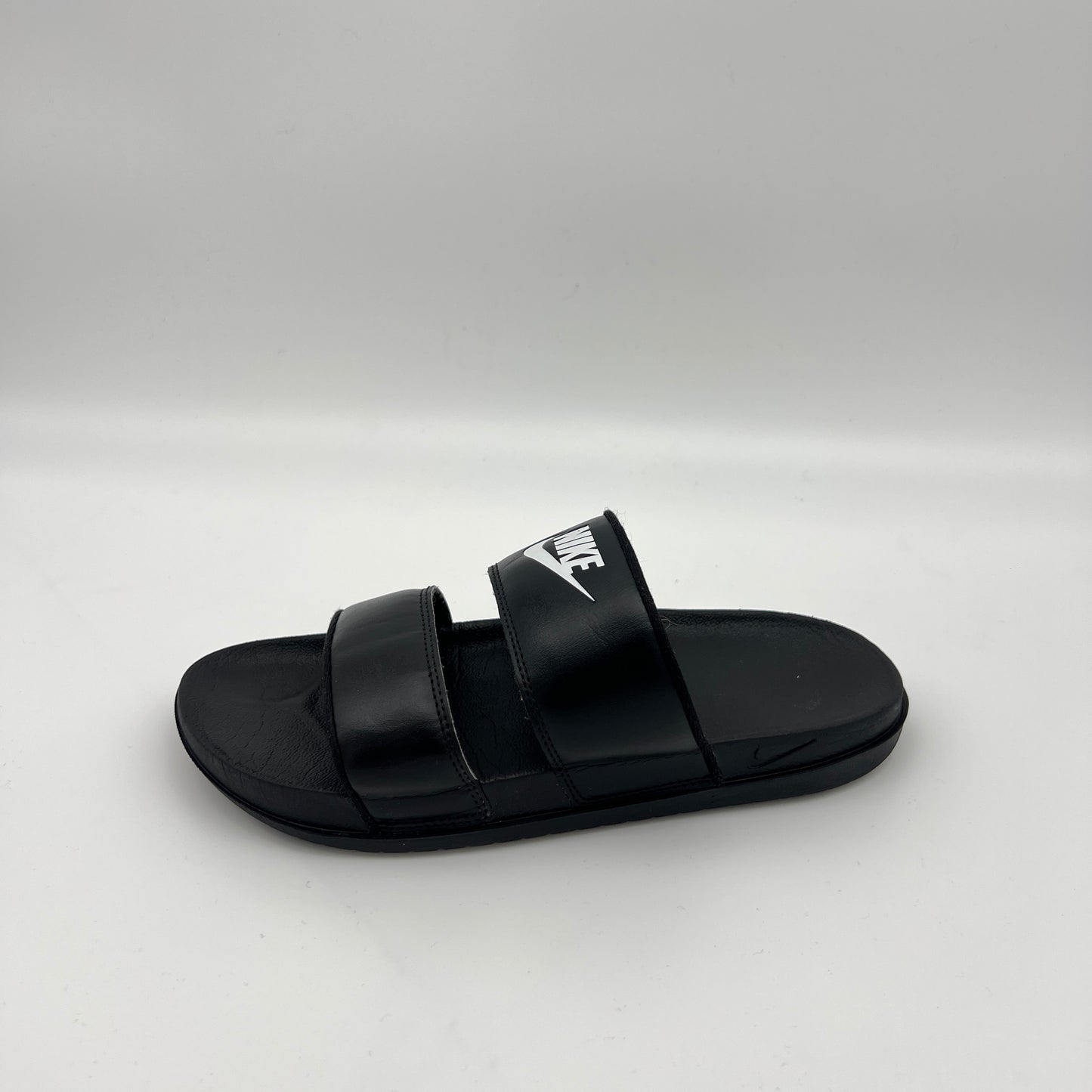A side-profile view of a black Nike Offcourt Duo slide sandal with two parallel synthetic straps, a white Nike wordmark on the top strap, and a contoured footbed
