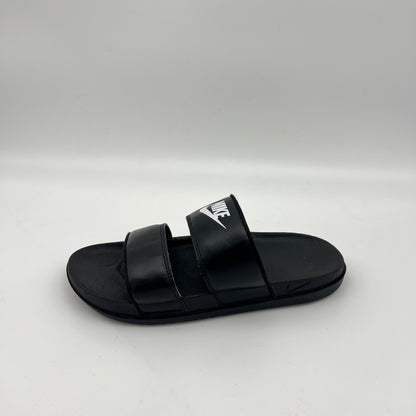 A side-profile view of a black Nike Offcourt Duo slide sandal with two parallel synthetic straps, a white Nike wordmark on the top strap, and a contoured footbed