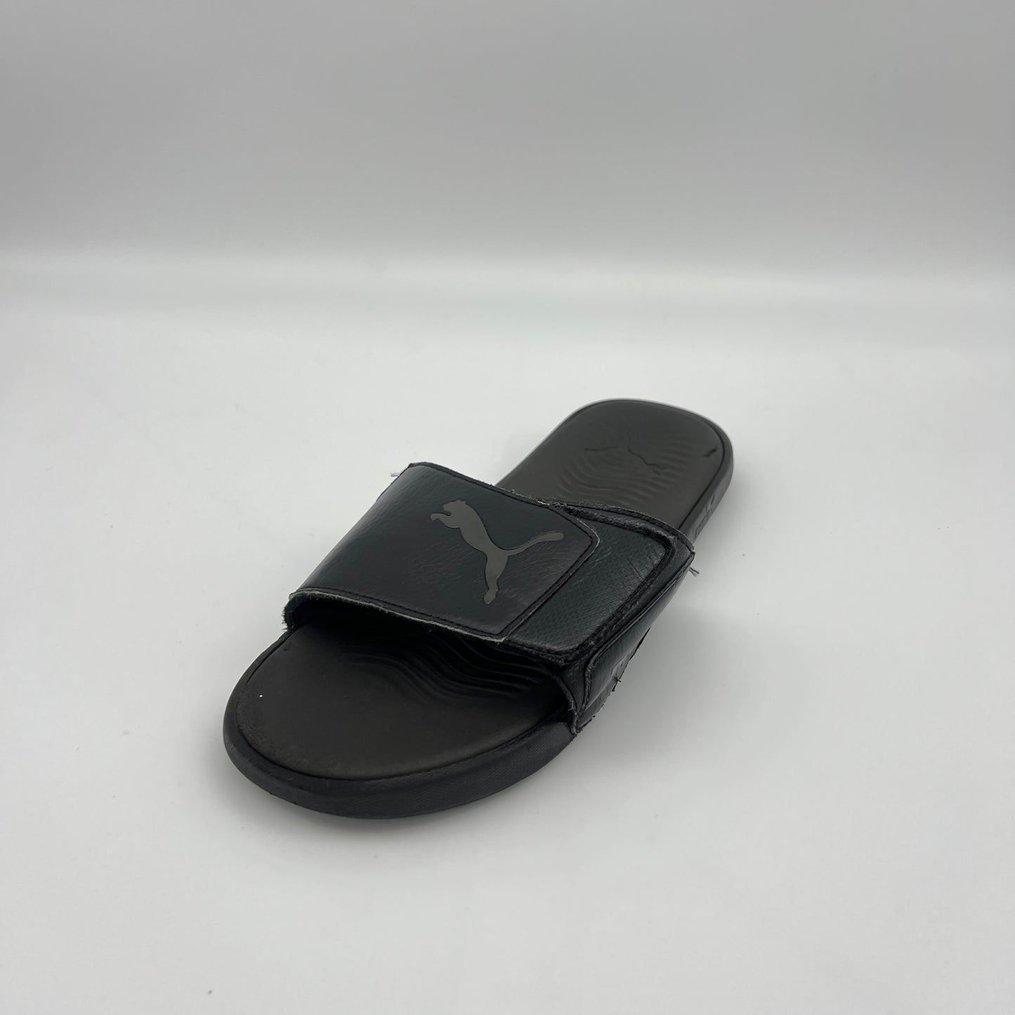Black slide sandal with Puma logo on a light gray background