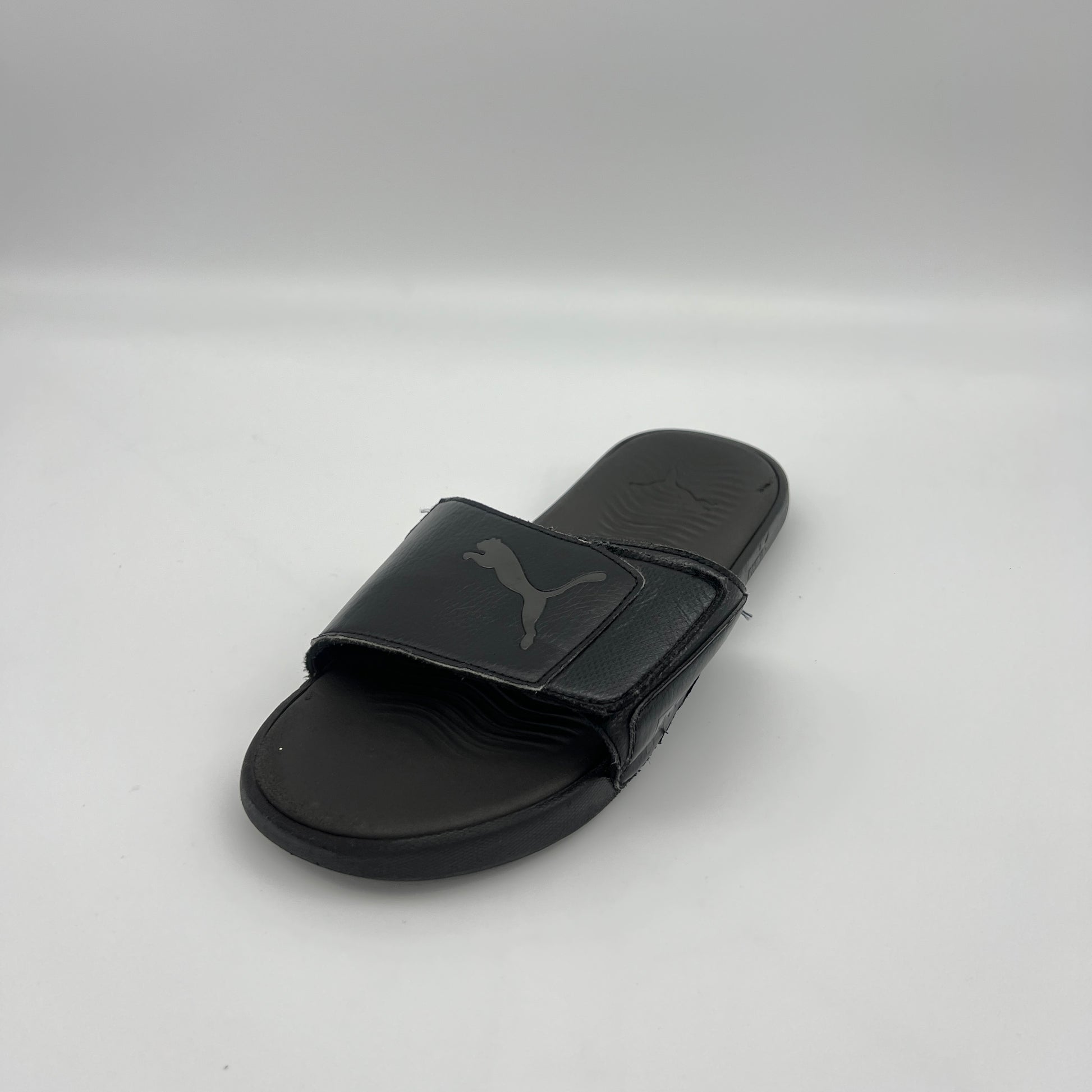 Black slide sandal with Puma logo on a light gray background