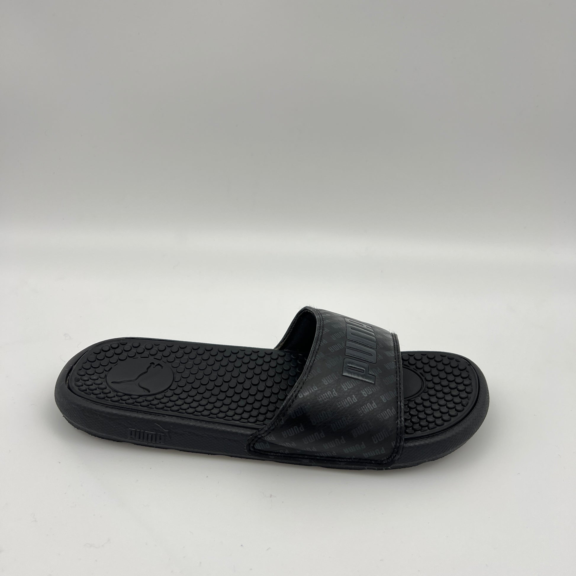 PUMA Cool Cat V slide in black featuring a repeating PUMA logo pattern on the strap and a textured, contoured black footbed.