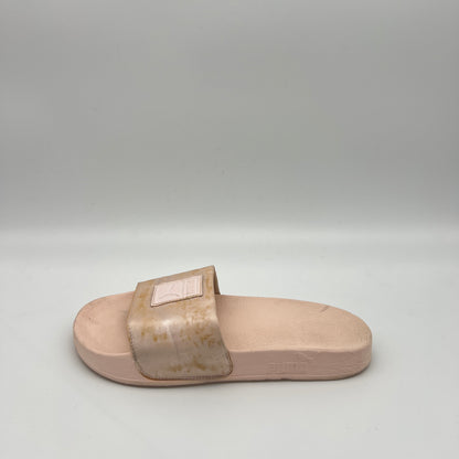Side view of a rose gold Puma Cool Cat Sport slide sandal for women featuring a metallic strap with a square logo patch and a pink cushioned footbed.
