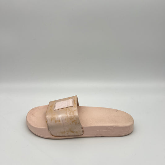 Side view of a rose gold Puma Cool Cat Sport slide sandal for women featuring a metallic strap with a square logo patch and a pink cushioned footbed.
