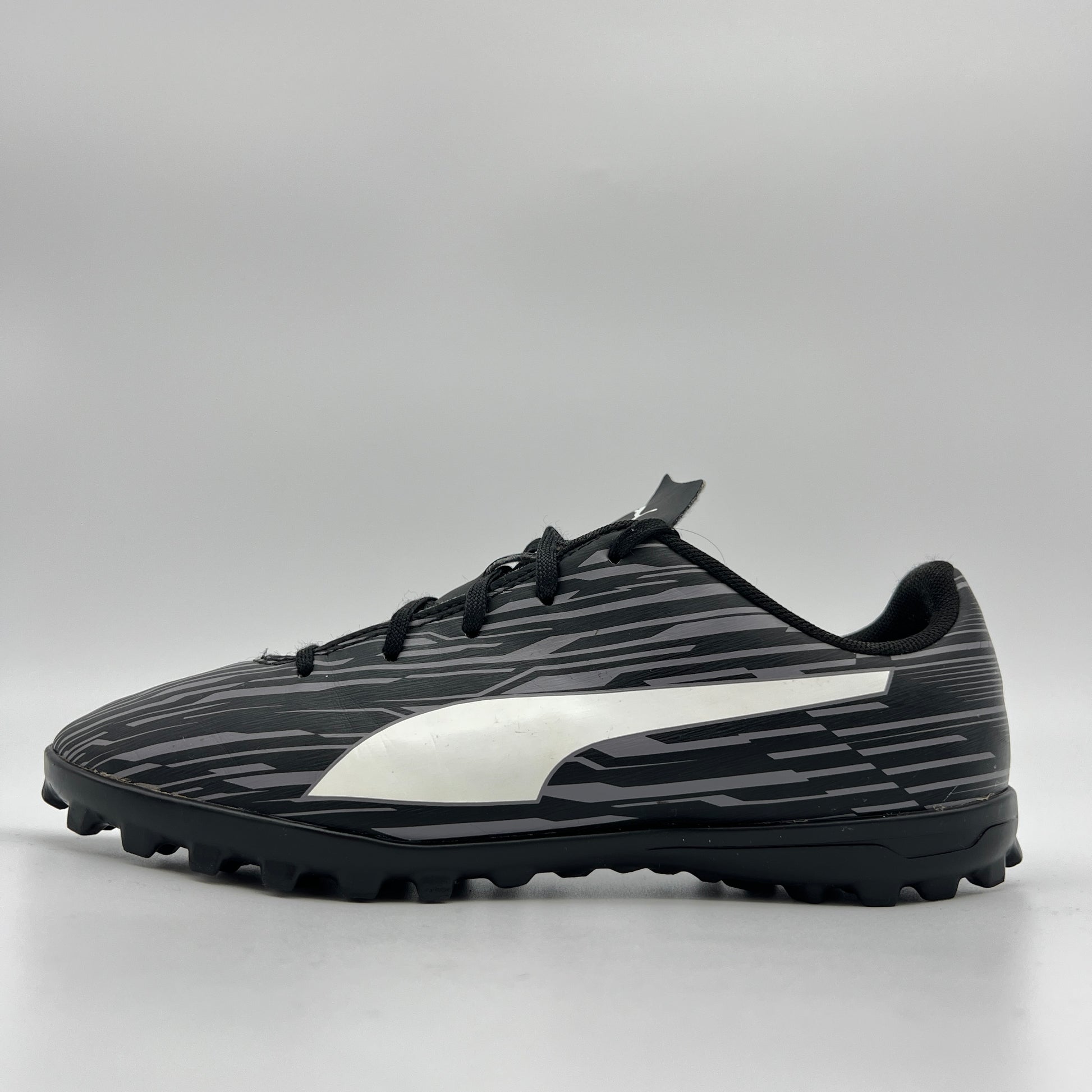 Side profile of a black Puma Rapido III TT soccer shoe featuring a grey-striped graphic pattern, white Puma formstrip, and black turf-ground studs.