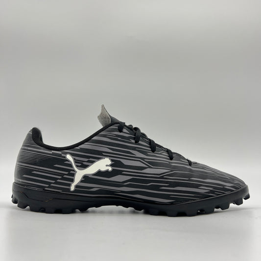 Side profile of a black Puma Rapido III TT soccer shoe featuring a grey-striped graphic pattern, white Puma formstrip, and black turf-ground studs.