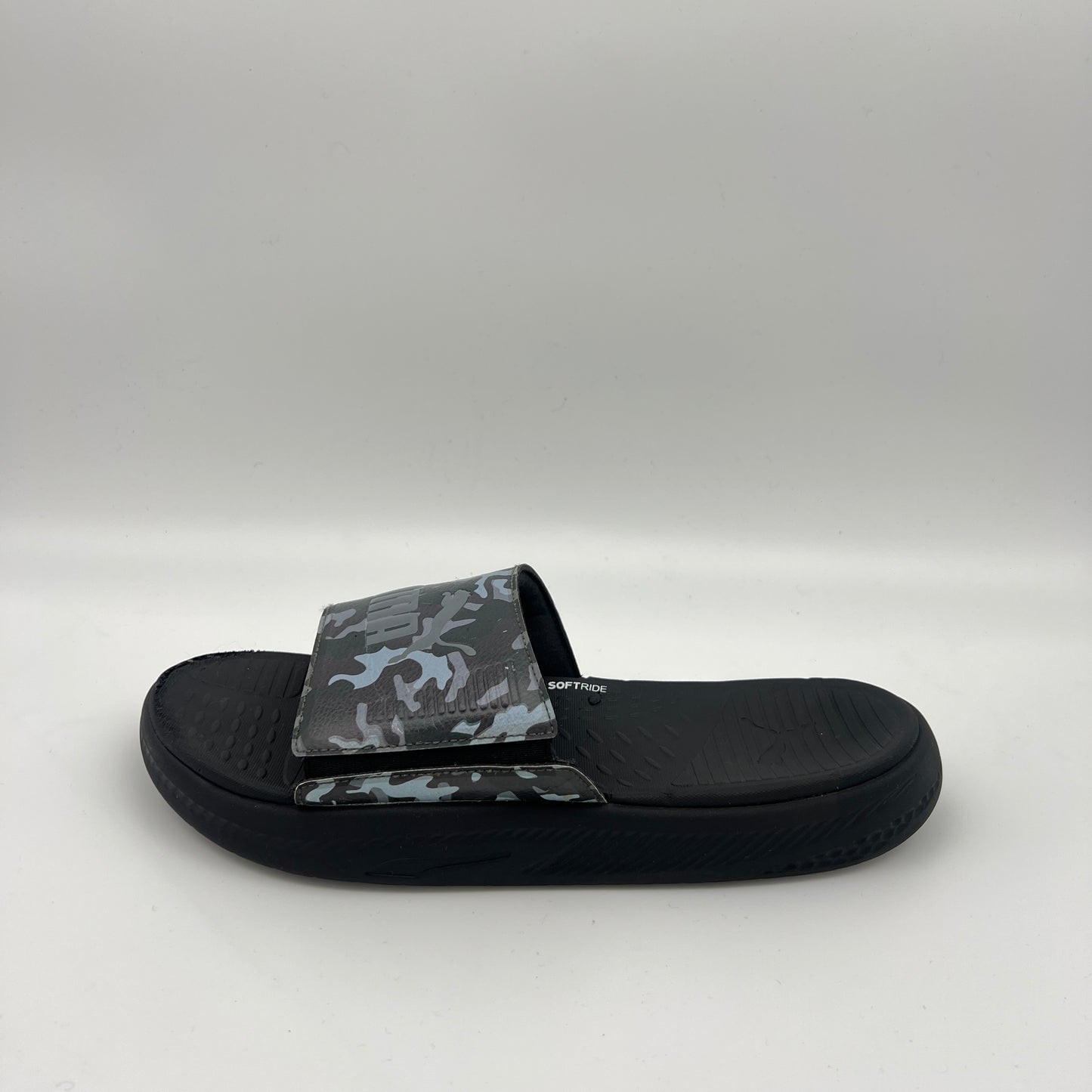 A side view of a black Puma Softride slide sandal featuring a grey and black camouflage patterned strap with an adjustable closure and a thick cushioned sole.