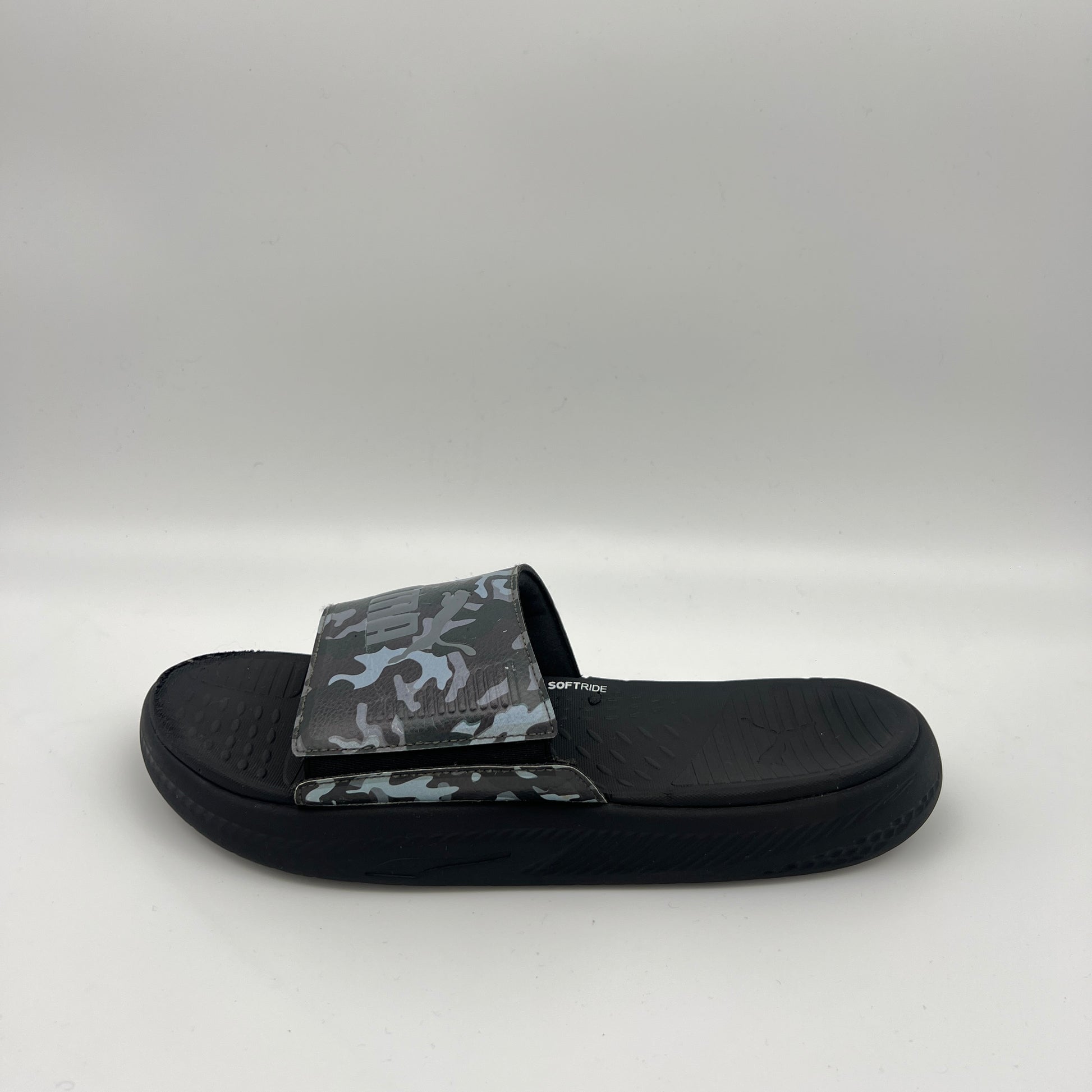 A side view of a black Puma Softride slide sandal featuring a grey and black camouflage patterned strap with an adjustable closure and a thick cushioned sole.