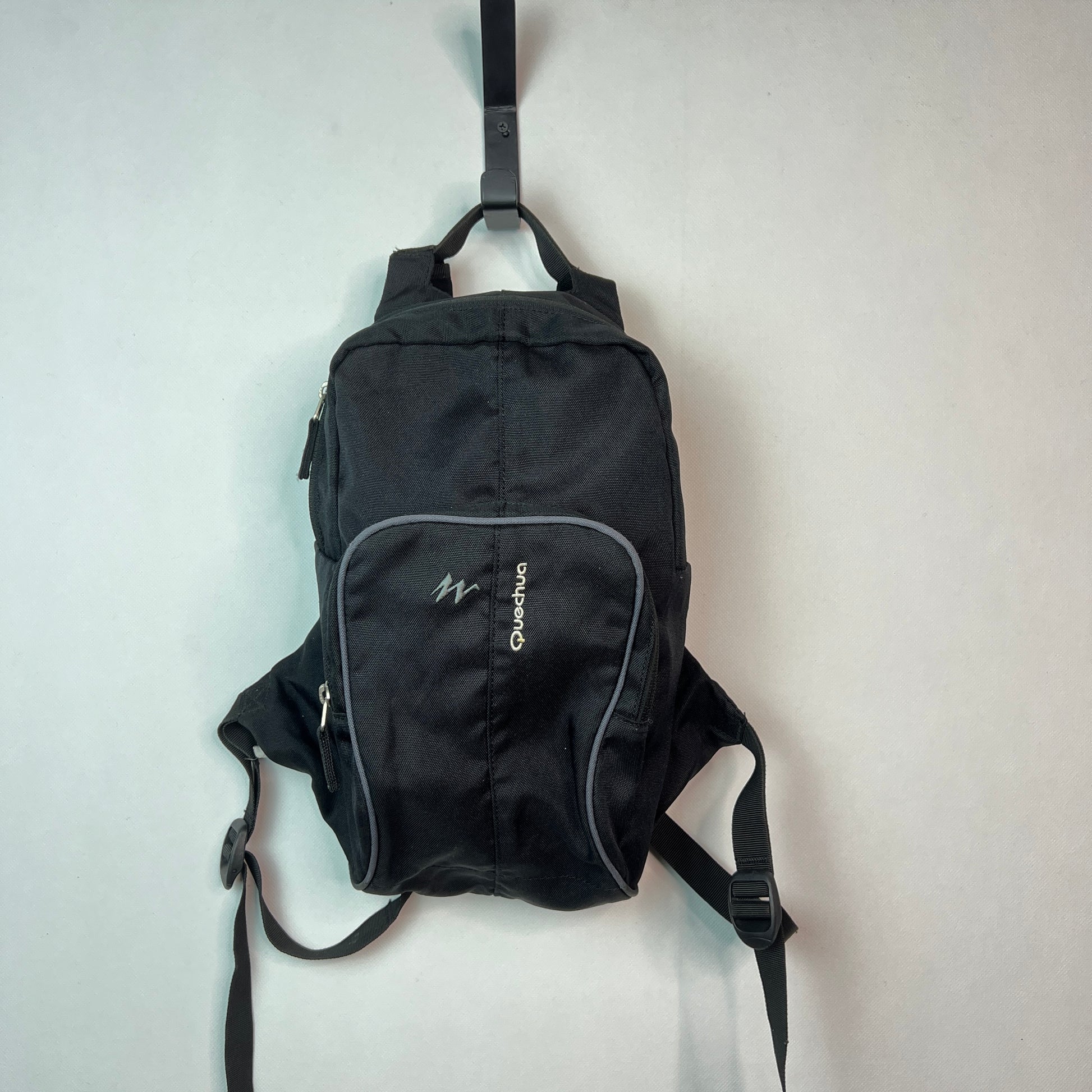 Black Quechua Arpenaz 10L backpack with grey piping on the front pocket hanging on a hook.