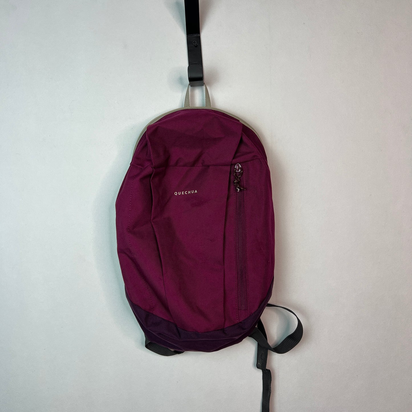Purple Quechua NH100 10L hiking backpack hanging on a wall hook