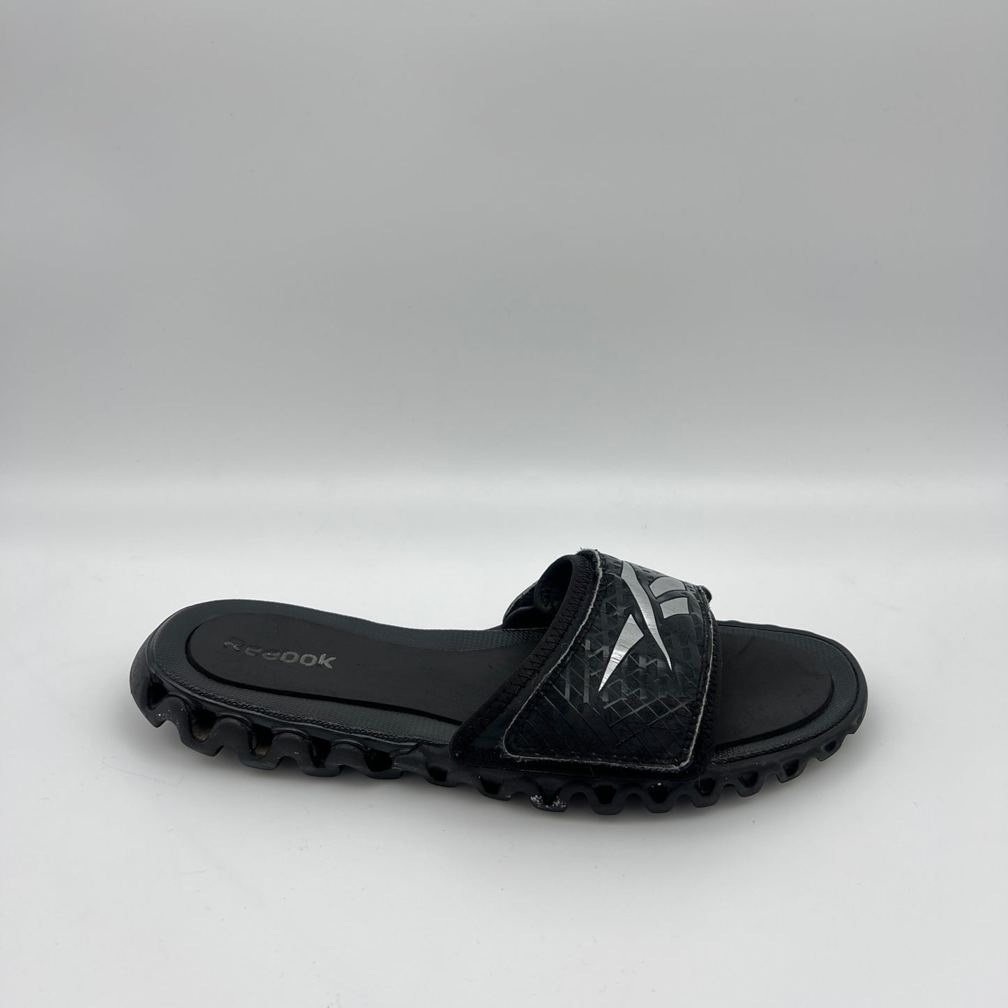 Reebok Zig Nano Slide black and silver athletic sandal with zigzag cushioning sole and adjustable logo strap.