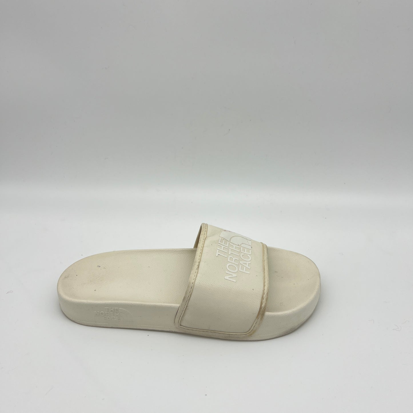 Side view of an off-white The North Face Base Camp Slide III with a textured "THE NORTH FACE" logo on a wide synthetic strap and a contoured cream footbed.