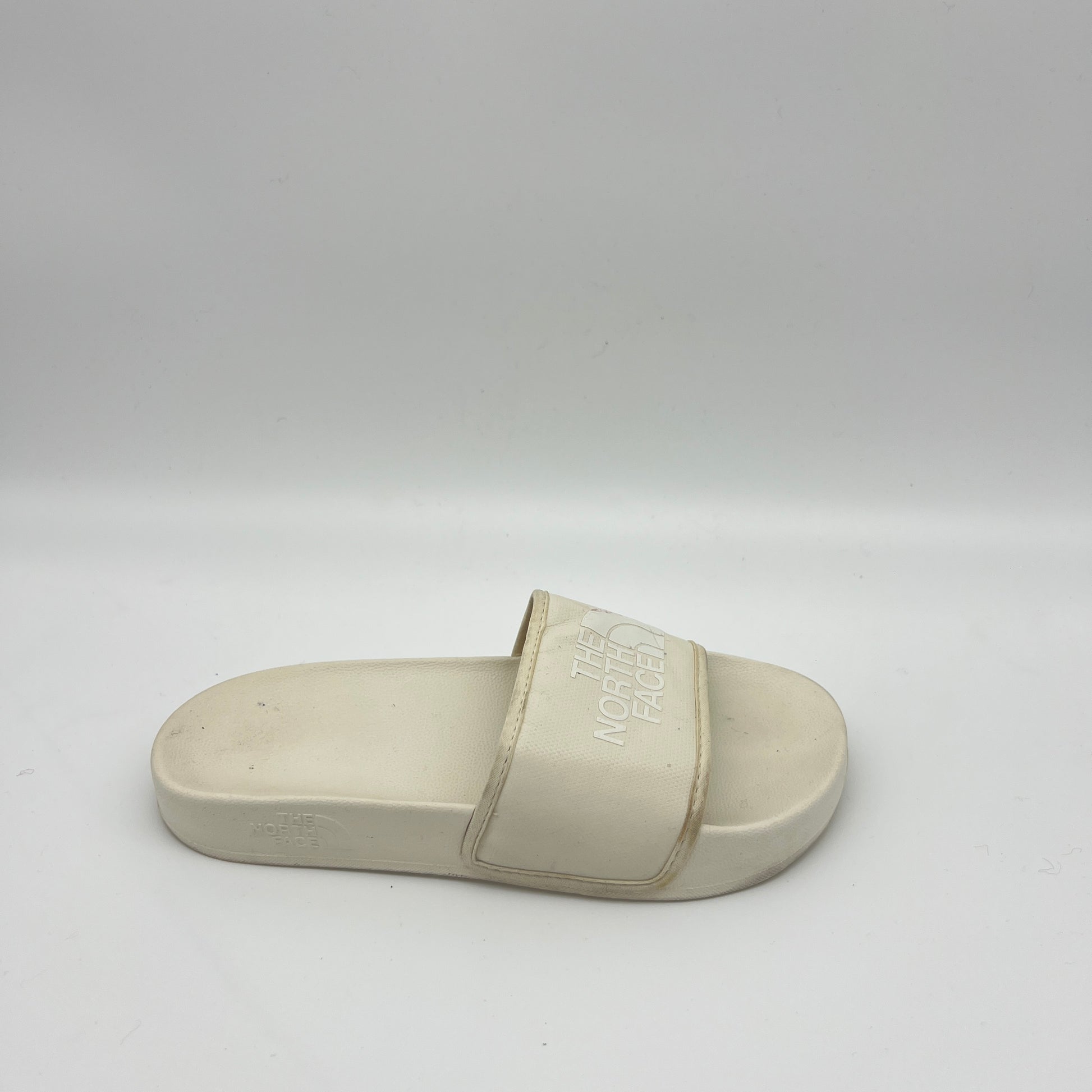 Side view of an off-white The North Face Base Camp Slide III with a textured "THE NORTH FACE" logo on a wide synthetic strap and a contoured cream footbed.