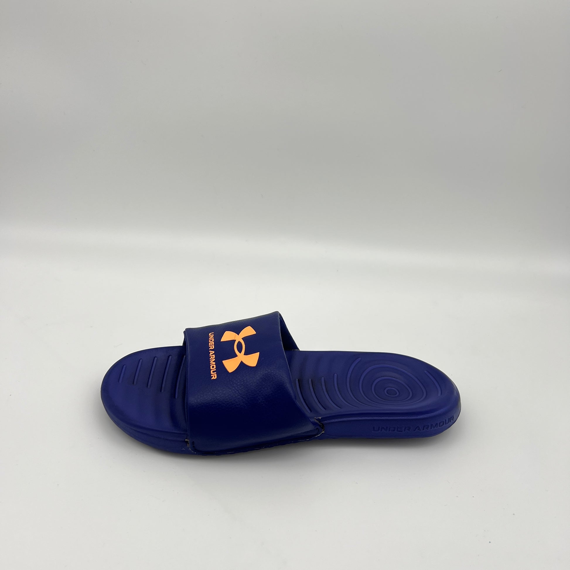 A single royal blue Under Armour Ansa Fixed slide sandal with a bright orange logo on the strap, displayed against a clean white background.