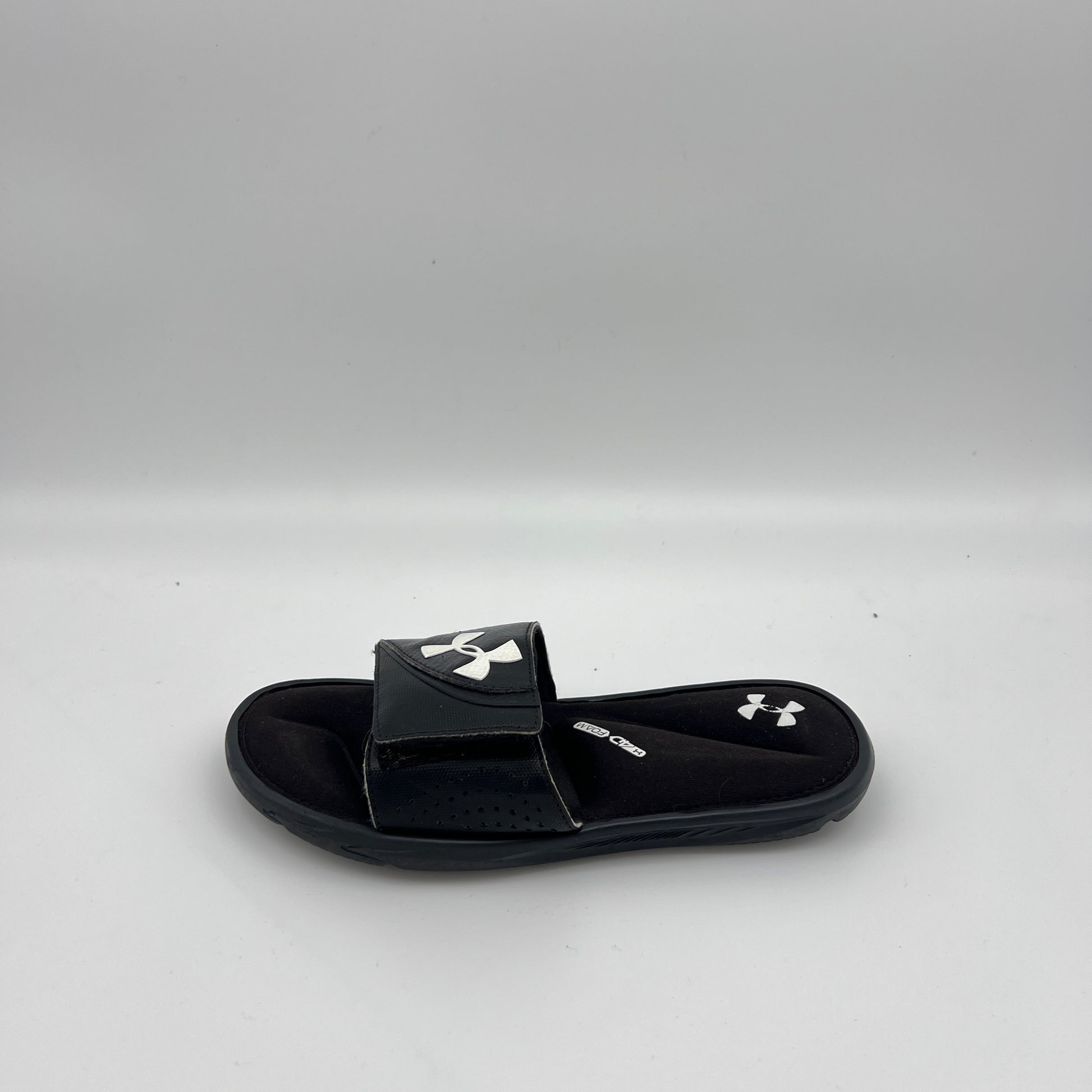Side view of Under Armour Men's Ignite VI slide in black and white with a contoured 4D Foam footbed