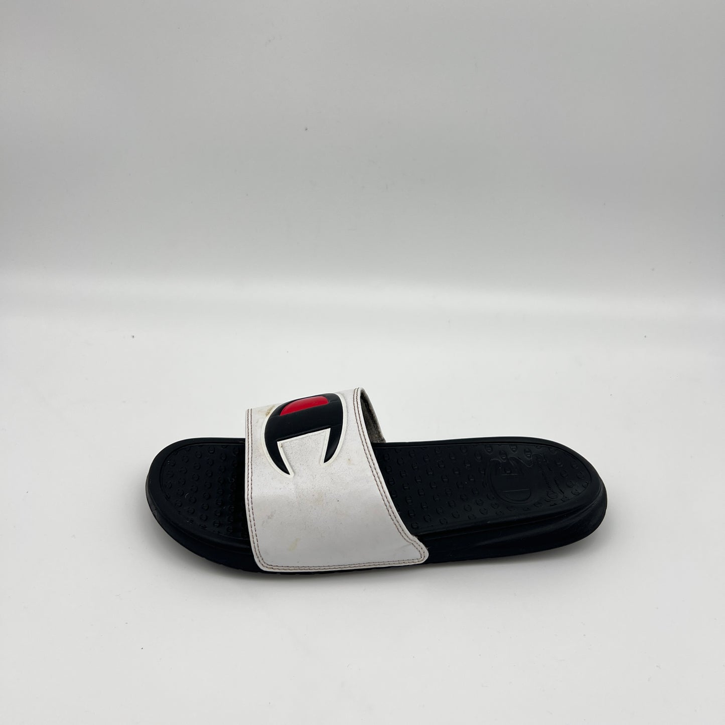 White Champion IPO slide sandal with big black and red "C" logo on a black footbed