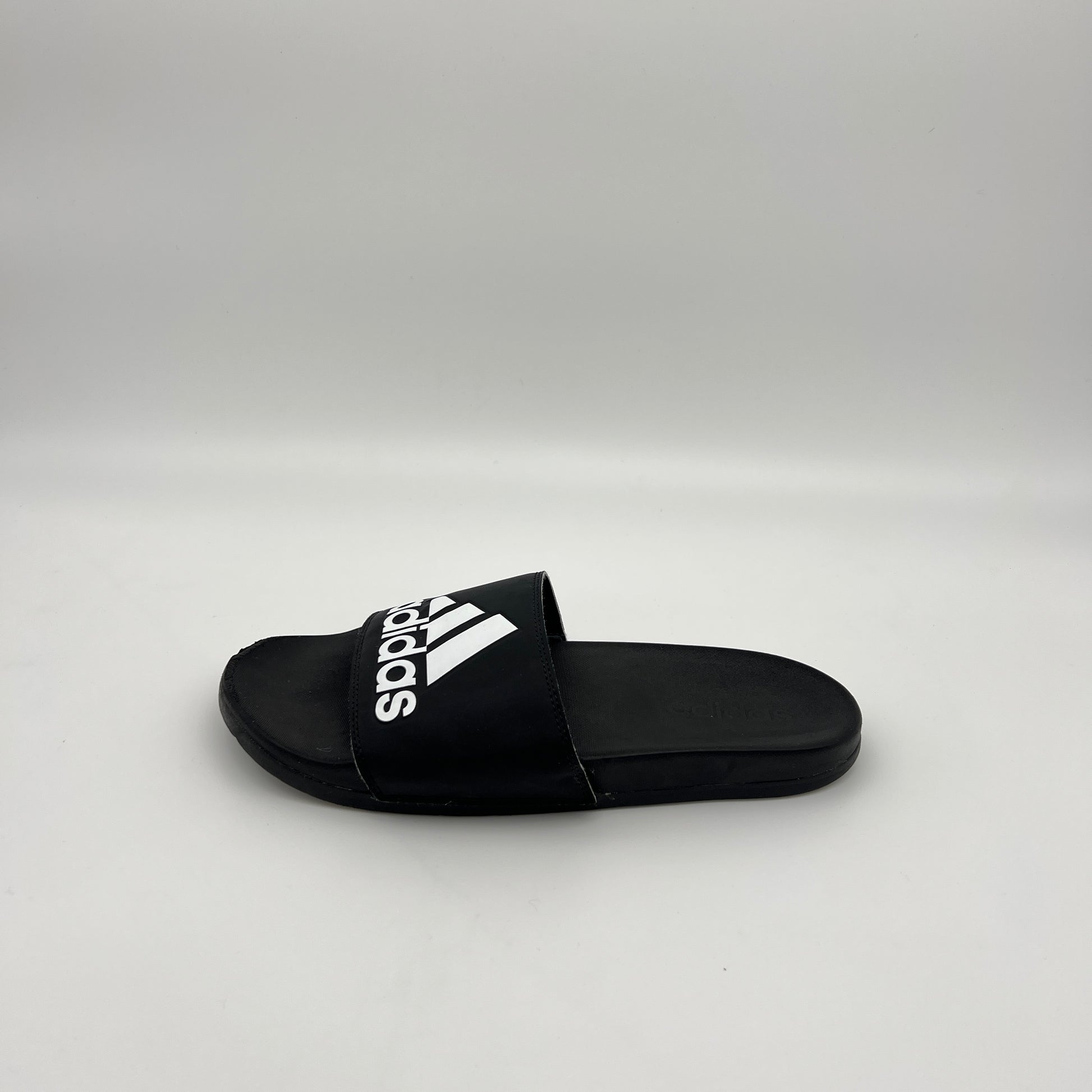 Profile view of a black Adidas Adilette Comfort slide with a white Badge of Sport logo on a clean white background