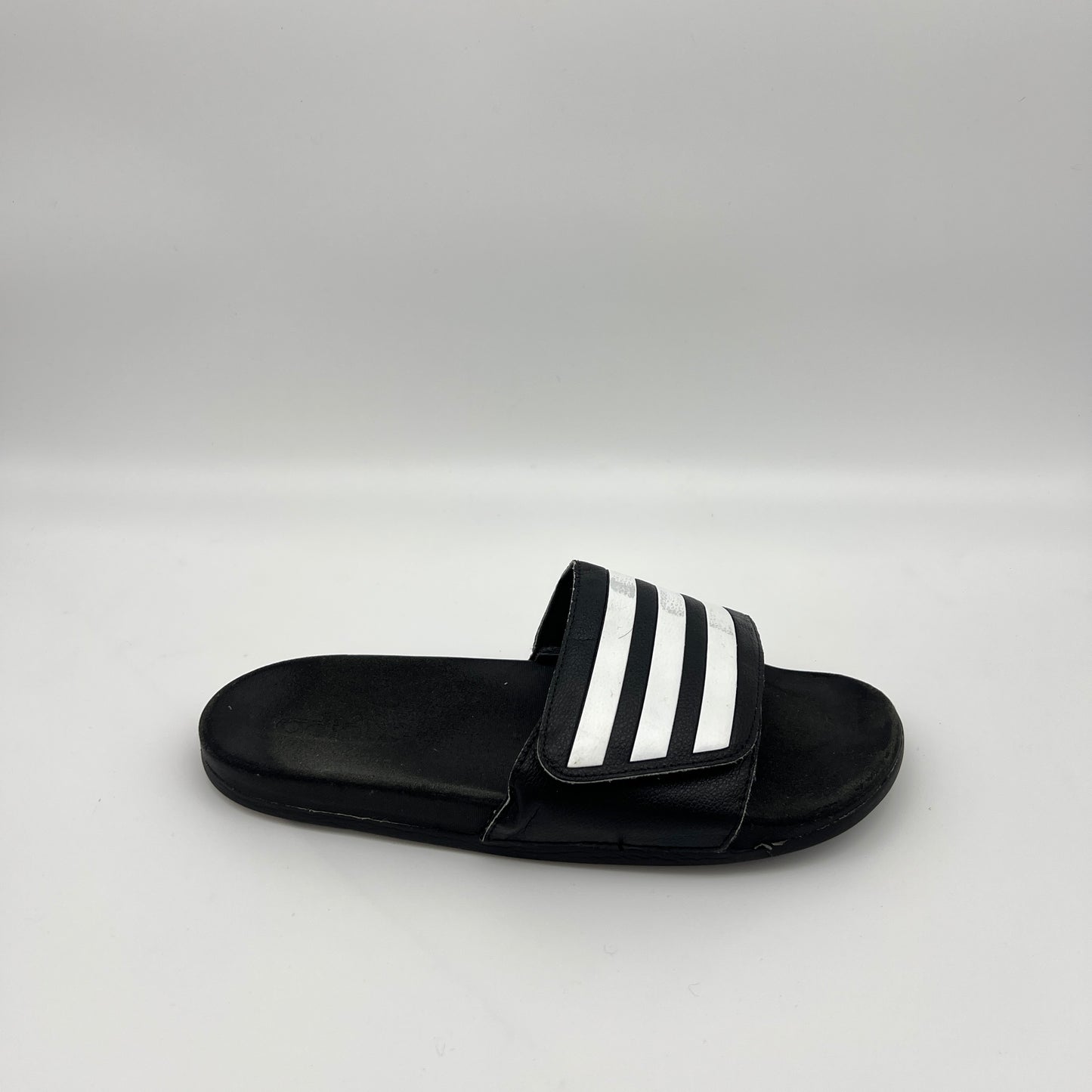 Side profile of a single black adidas Adilette slide sandal with three white iconic stripes on the strap and a smooth footbed on a plain white background.
