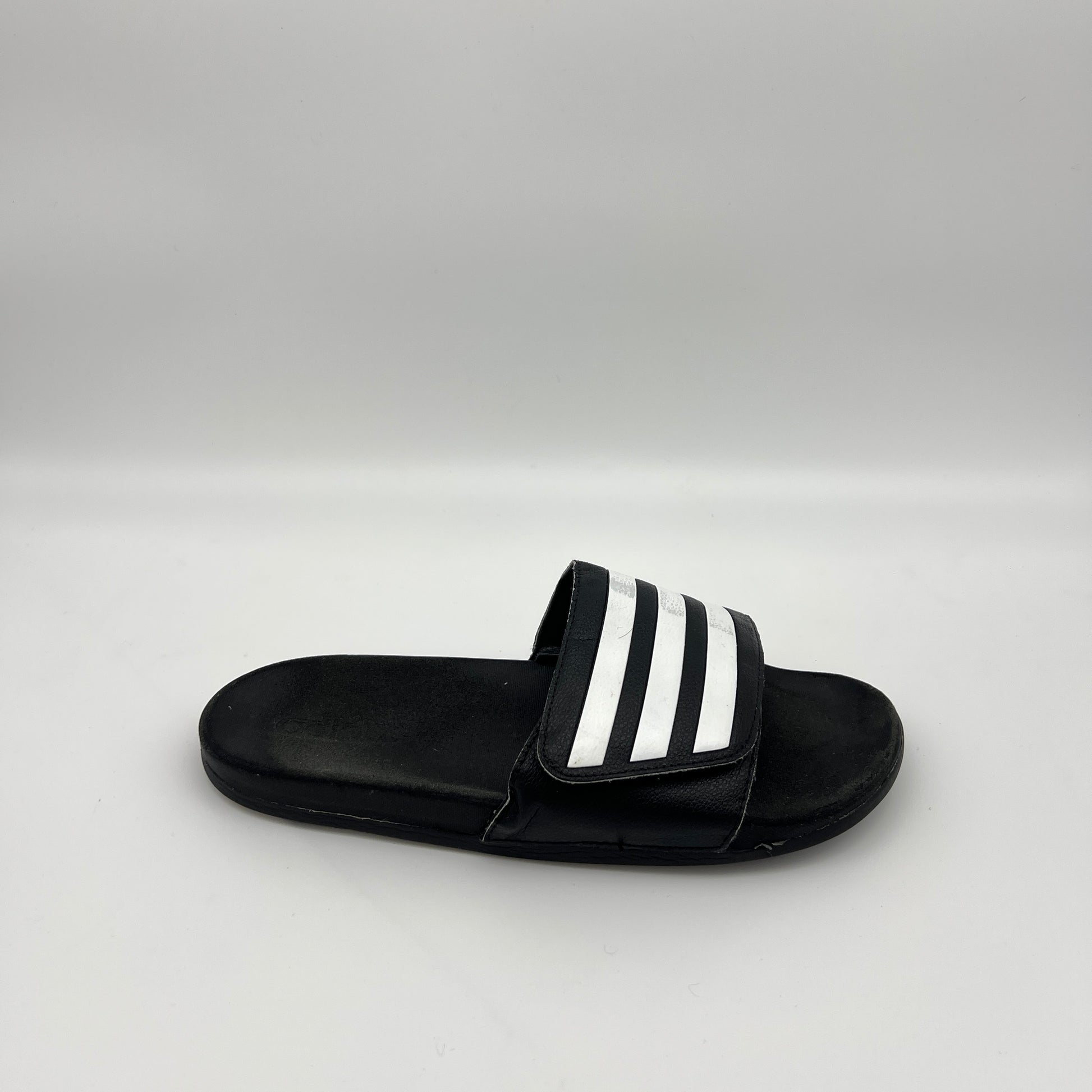 Side profile of a single black adidas Adilette slide sandal with three white iconic stripes on the strap and a smooth footbed on a plain white background.