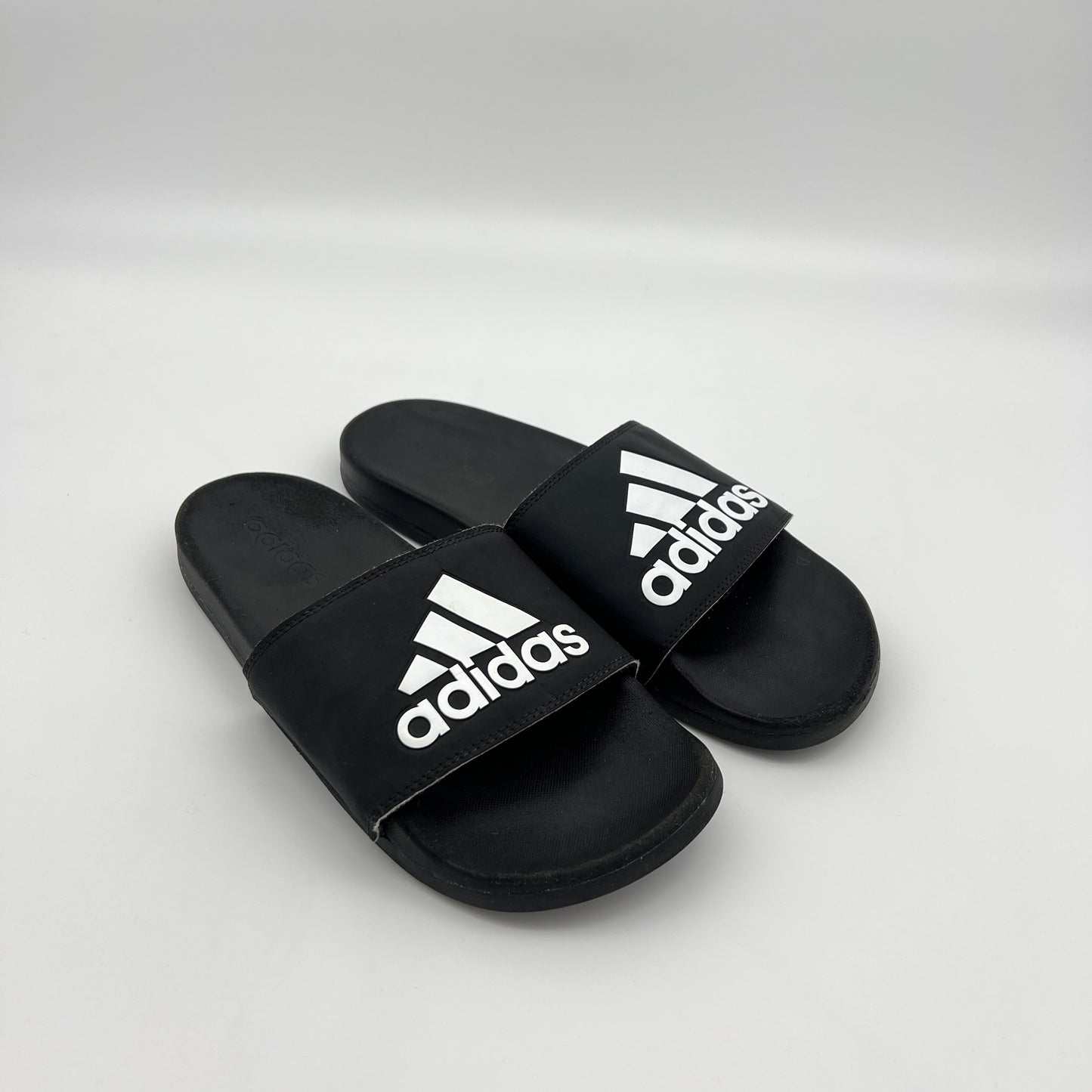 A person wearing black and white Adidas Adilette Comfort slides for casual everyday use.