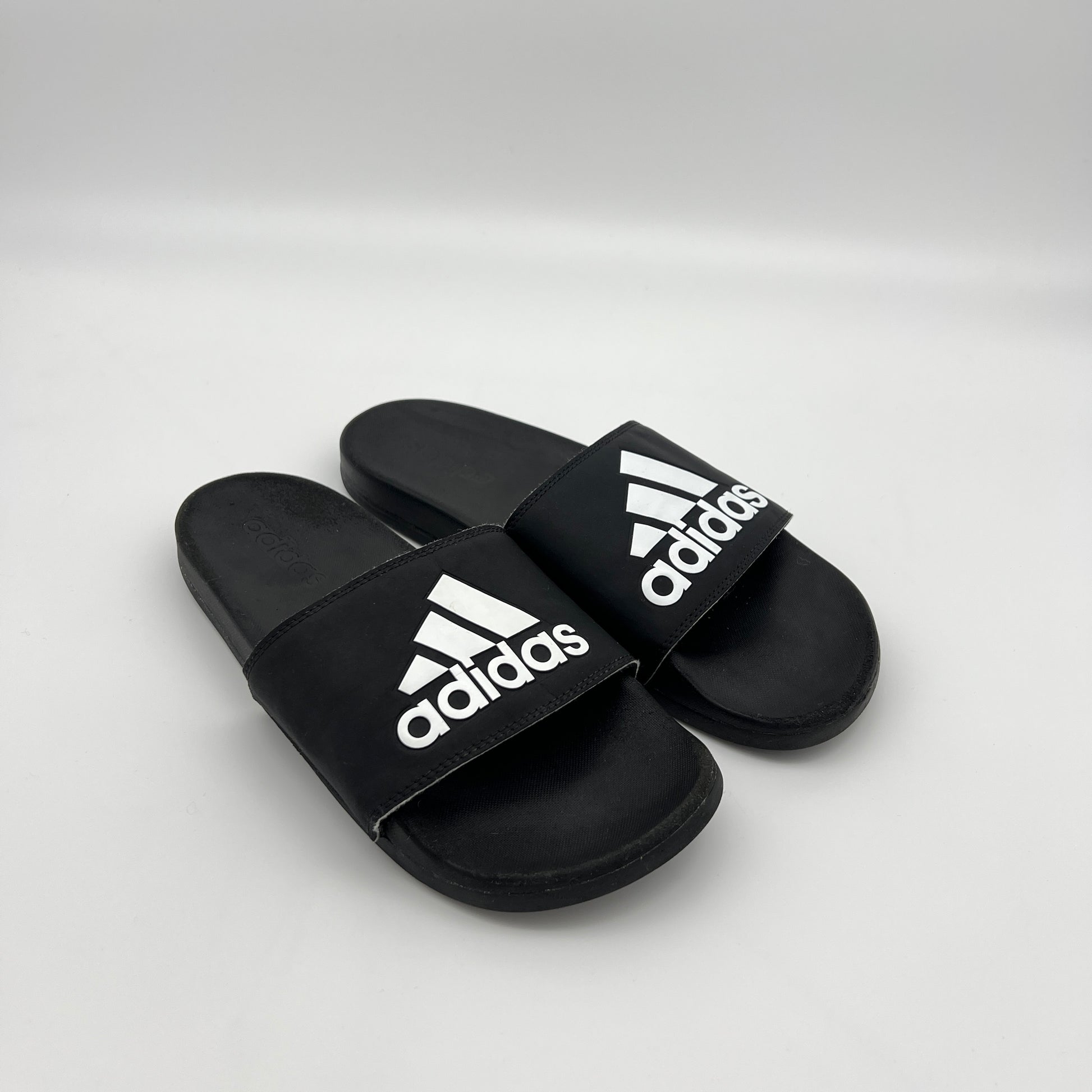 A person wearing black and white Adidas Adilette Comfort slides for casual everyday use.