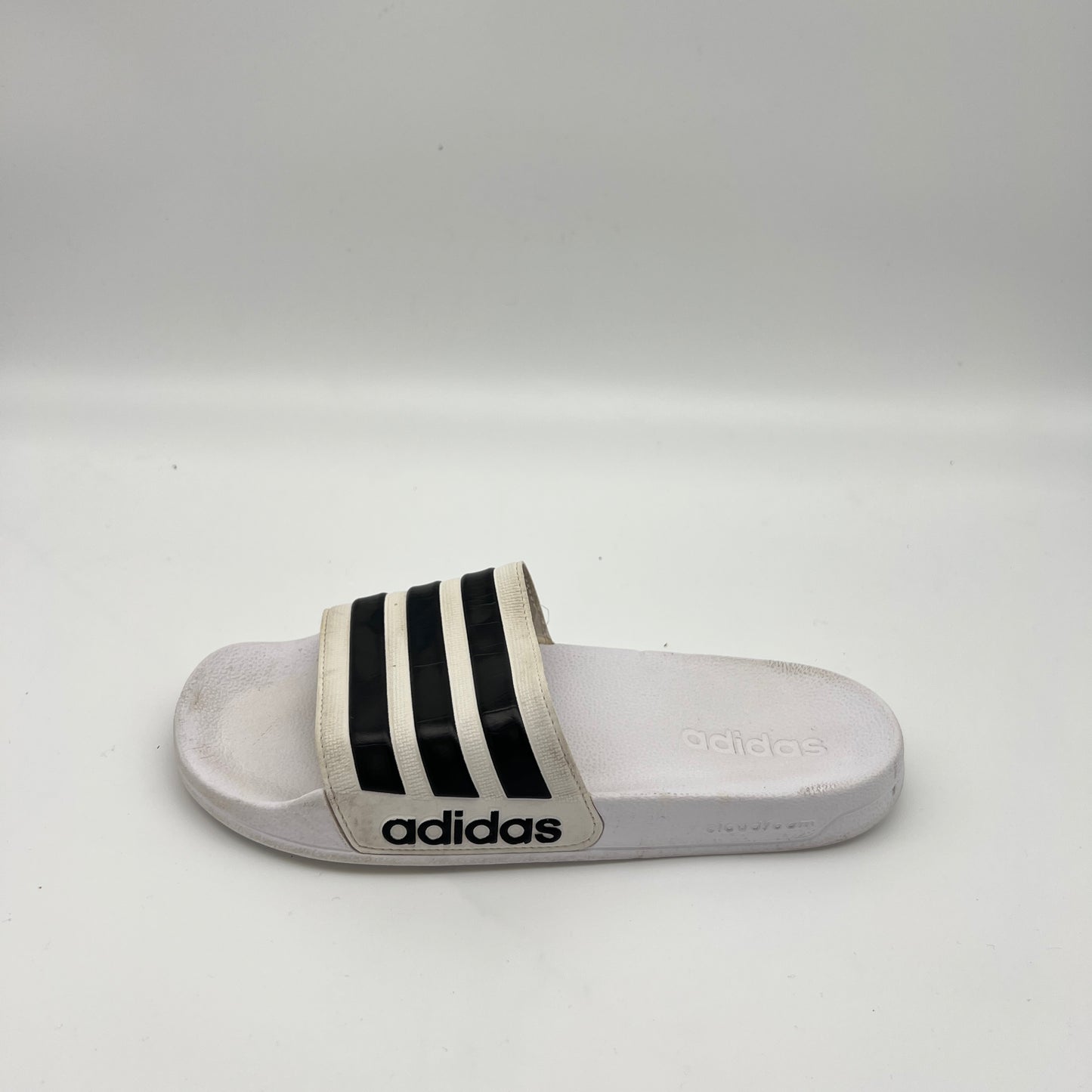 White adidas Adilette Shower slide sandal featuring three bold black stripes on the strap and a black adidas logo on the side of the sole