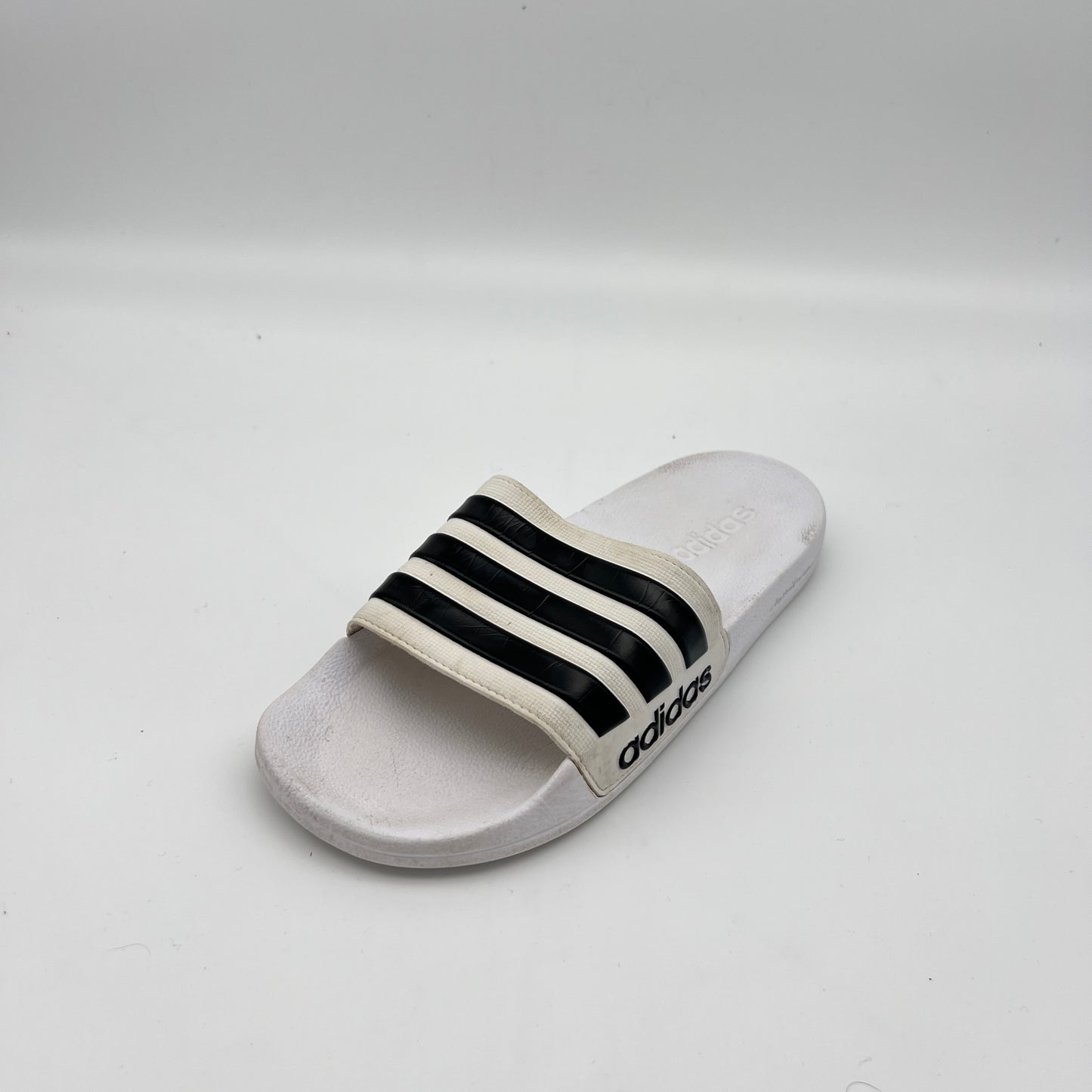 White slide sandal with black stripes on a light gray background