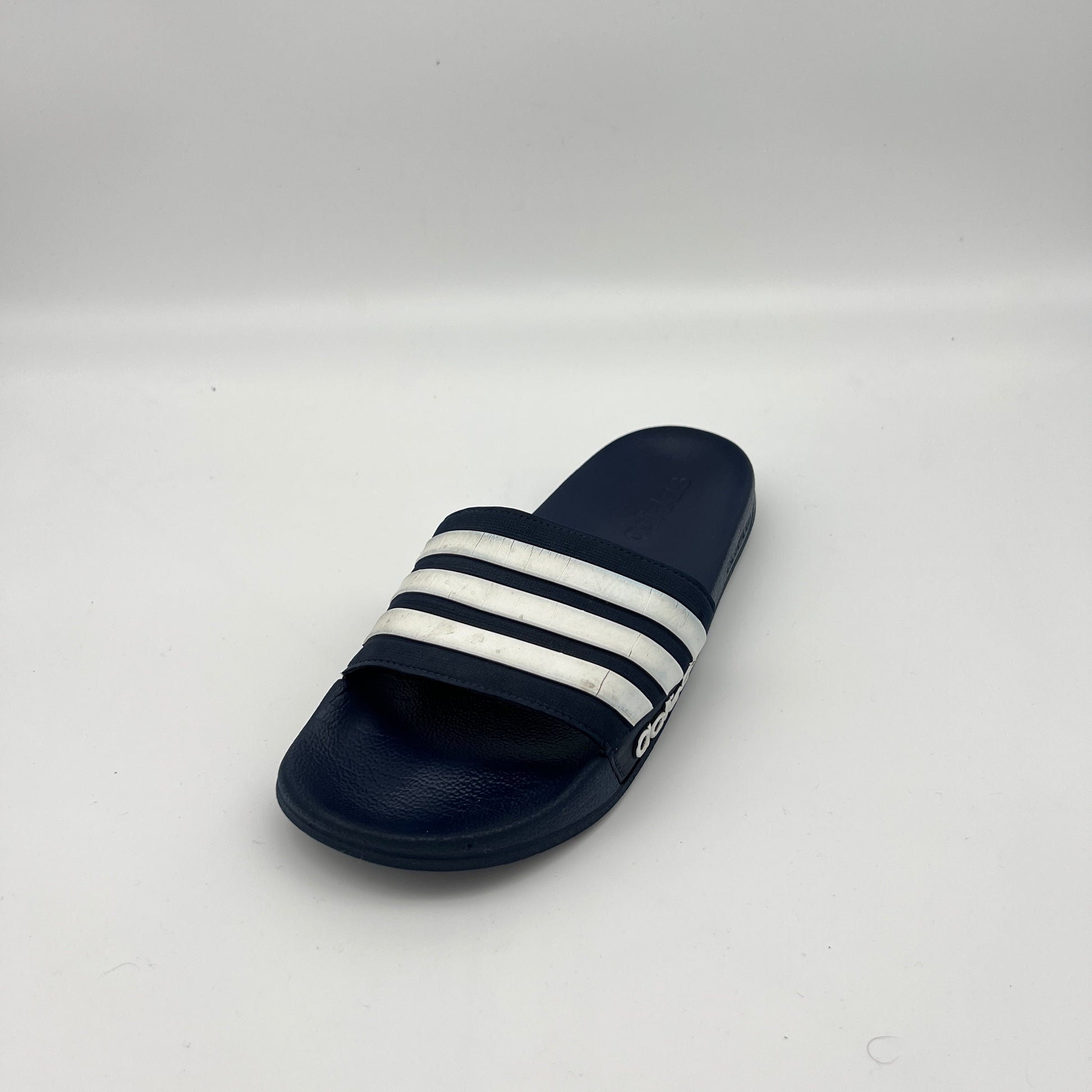 Navy blue slide sandal with white stripes on a light gray background
