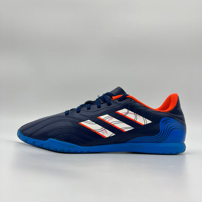 Side profile of a navy blue adidas Copa Sense.4 IN indoor football shoe with white stripes and bright orange interior lining against a plain grey background.