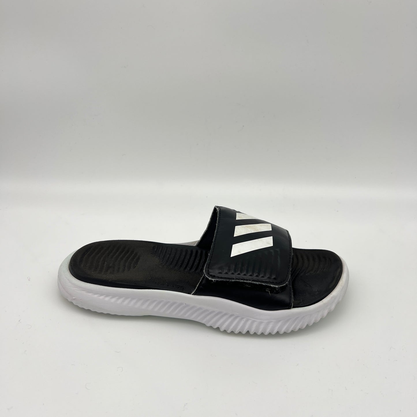 A side-angle view of a black adidas Alphabounce Slide 2.0 sandal featuring a white 3-Bar logo on an adjustable Velcro strap and a thick white Bounce sole.