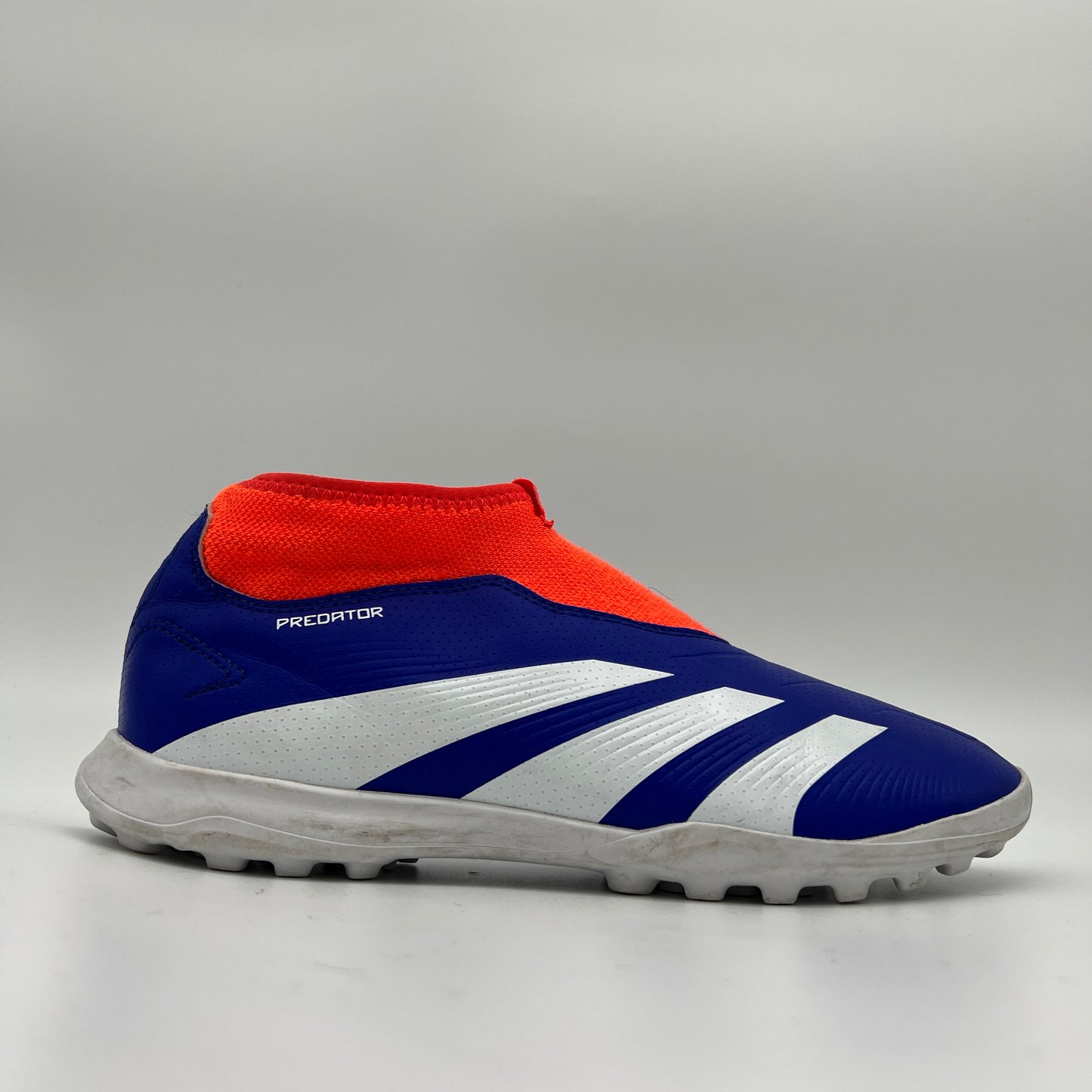 Side view of an adidas Predator League laceless turf soccer boot in lucid blue, footwear white, and solar red with a white lugged rubber outsole.