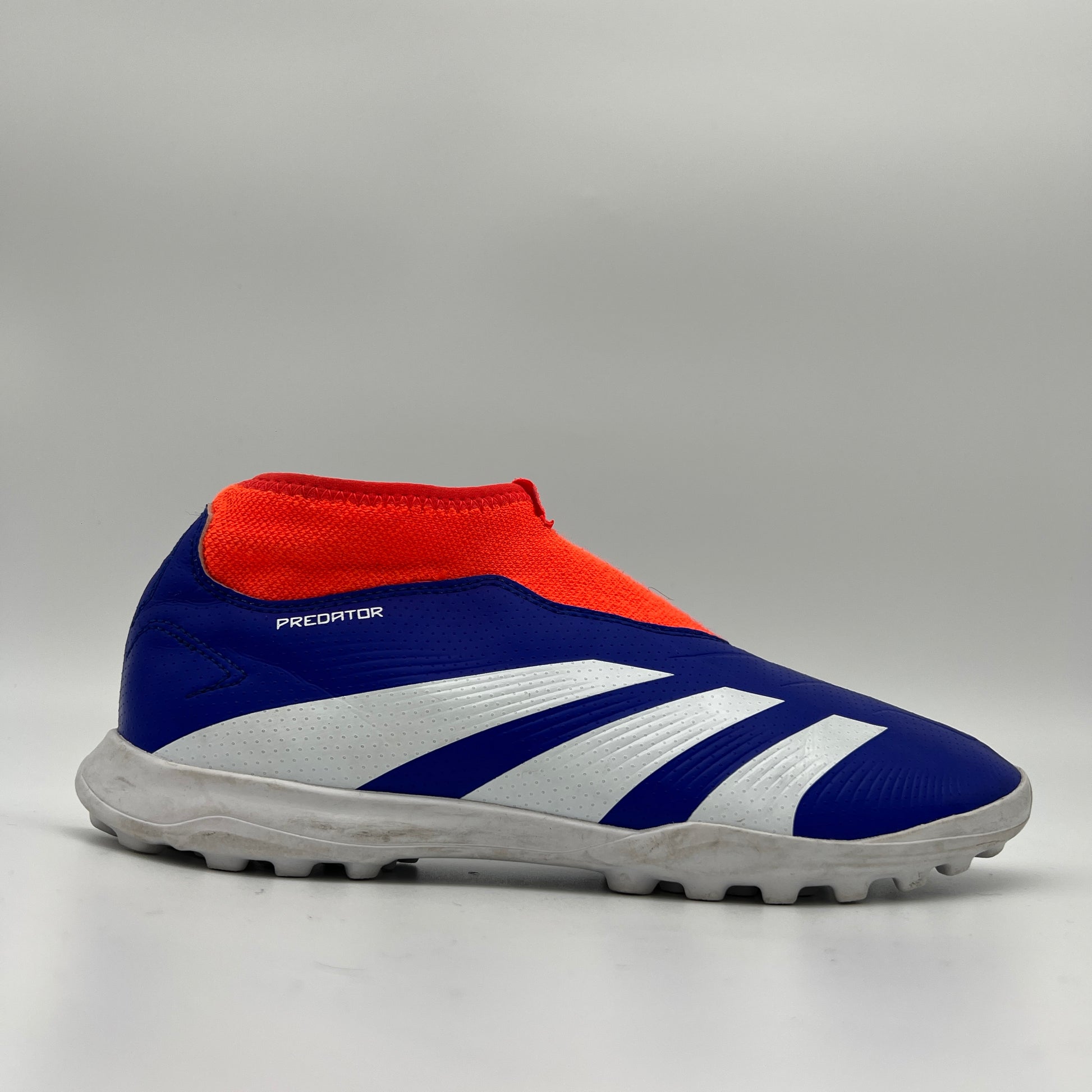 Side view of an adidas Predator League laceless turf soccer boot in lucid blue, footwear white, and solar red with a white lugged rubber outsole.