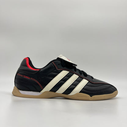 Side view of black Adidas Torra V IN J indoor soccer shoes with white stripes, red accents, and a gum rubber sole on a plain gray background.