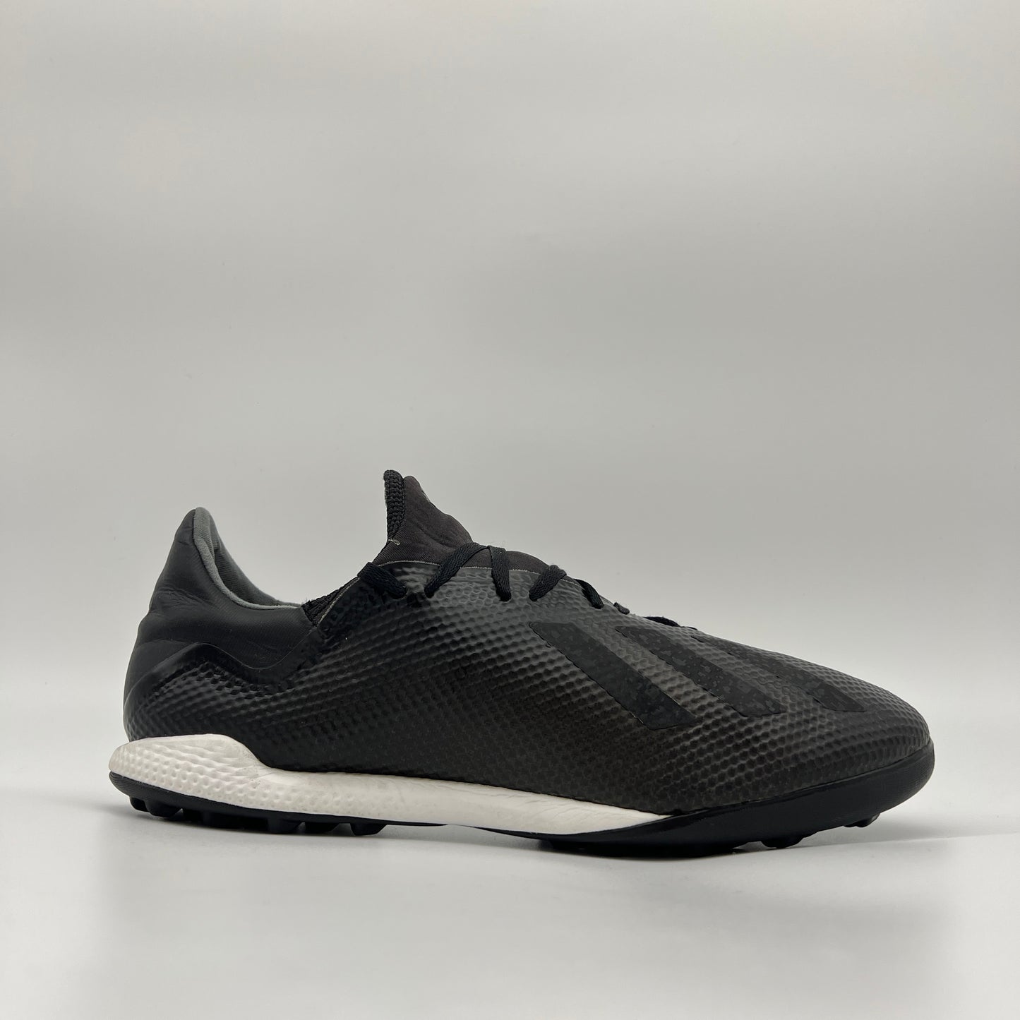 Side profile of a core black adidas X Tango 18.3 TF turf soccer shoe with a white midsole and black studded outsole for synthetic surfaces.
